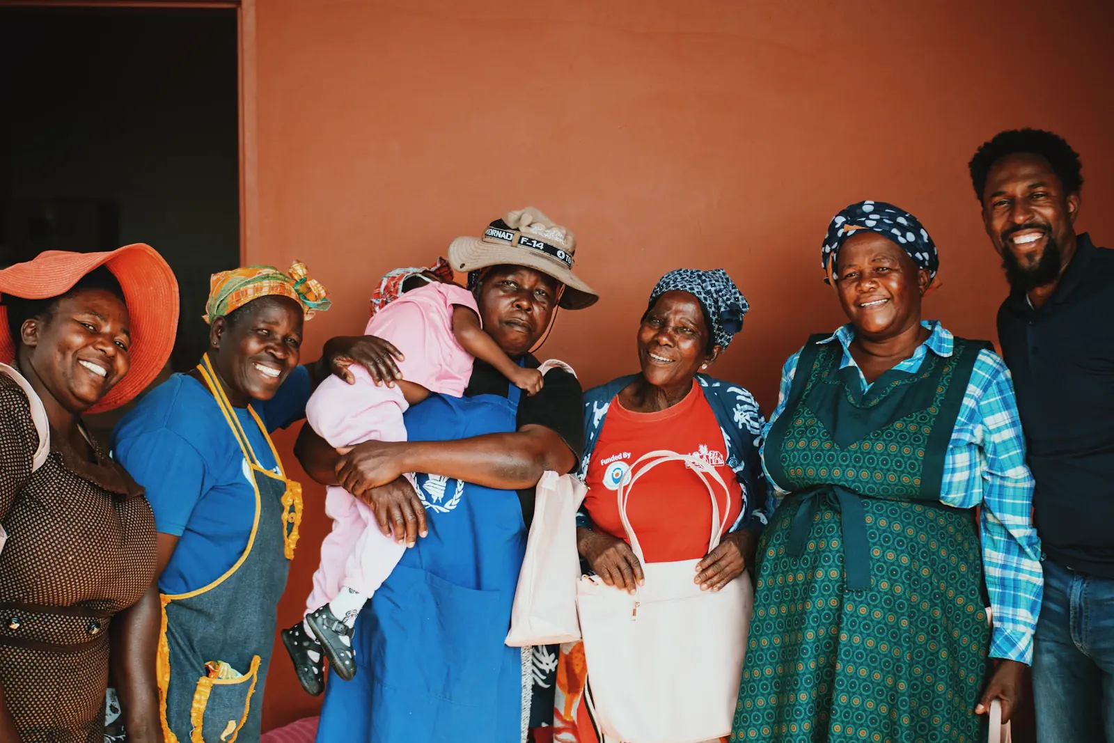 A group of women and a man smile together around a young child.